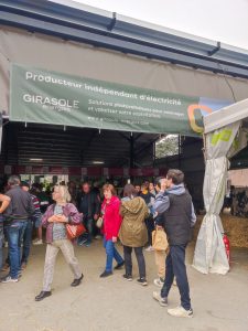Photo du stand Girasole Energies à la Foire de Réalmont, avec une bâche mentionnant « Producteur indépendant d’électricité » et des visiteurs déambulant dans l’espace d’exposition.